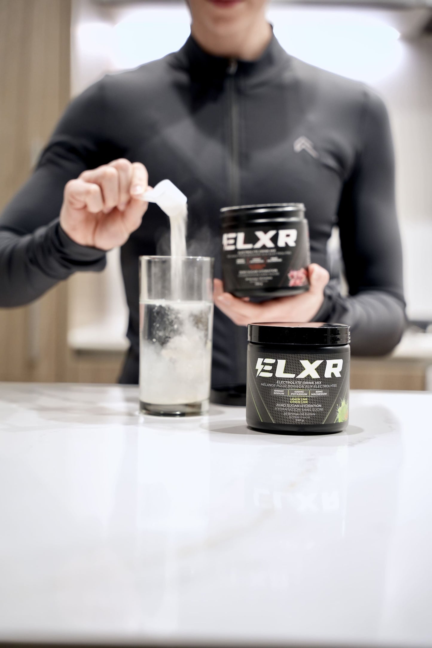 Person pouring a supplement into a glass with ELXR electrolytes containers in the foreground.