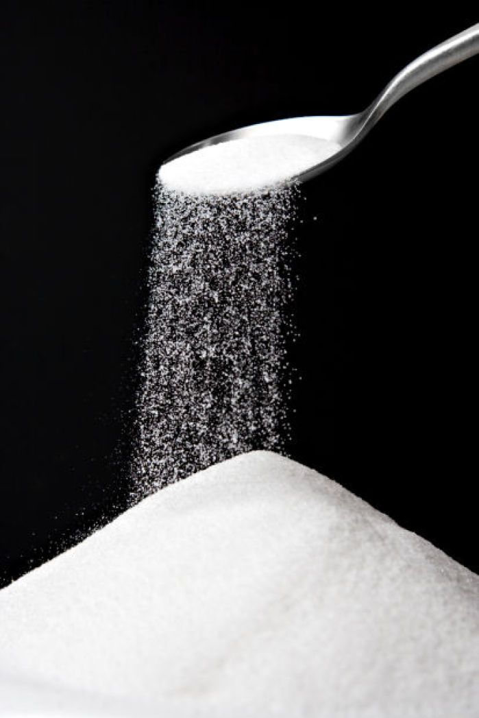 Spoon pouring sugar into a pile on a black background